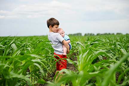 A boy holding a baby in a cornfield